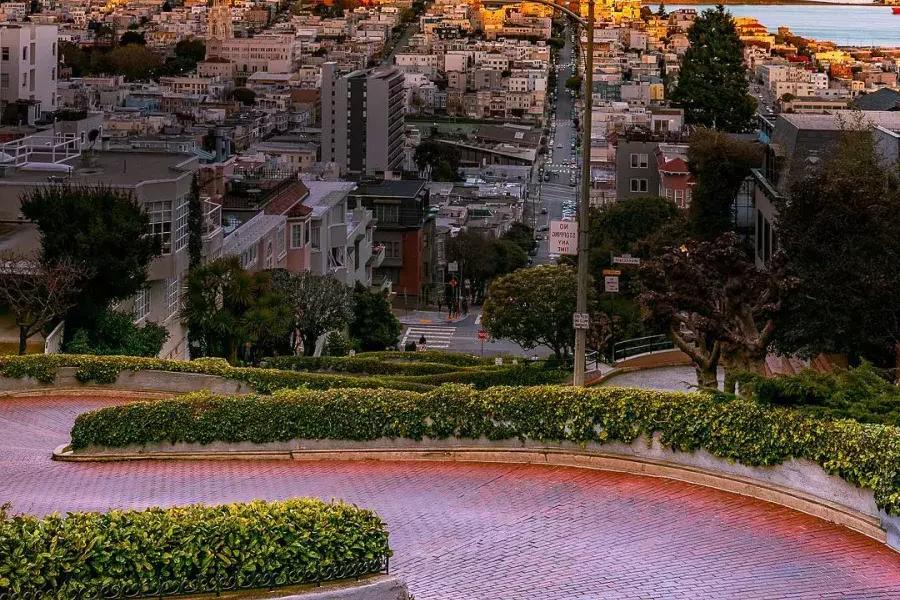 Lombard Street curves with Coit Tower in the distance during sunset.